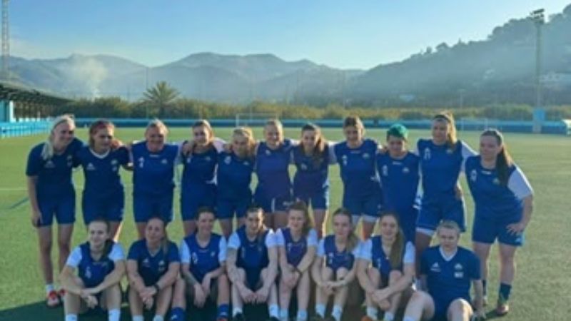Damfotbollslag samlat på en fotbollsplan under ett träningsläger i Spanien.